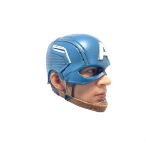 Puede incluir: Un casco de pl&aacute;stico azul y blanco de Captain America con una correa marr&oacute;n. El casco tiene una "A" blanca en el lateral.