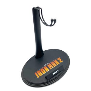 May include: Black plastic action figure stand with a metal hook. The stand has a circular base with the text "IRON MAN 2" and "MARK V" printed on it.