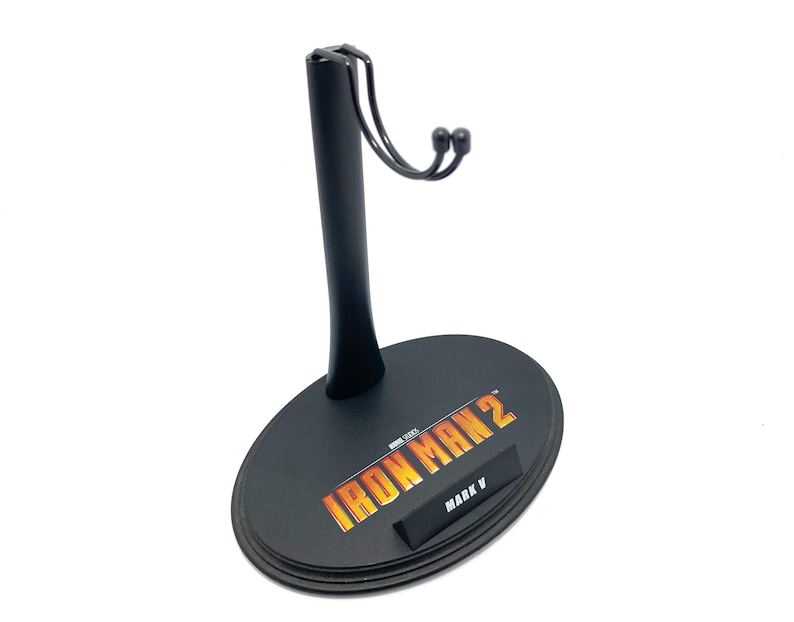 May include: Black plastic action figure stand with a metal hook. The stand has a circular base with the text "IRON MAN 2" and "MARK V" printed on it.