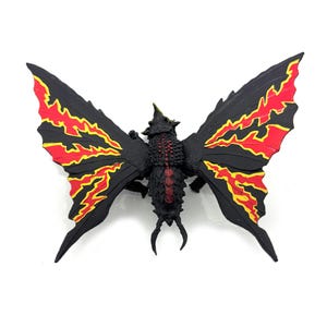 May include: A black creature figurine with large, wing-like appendages featuring vibrant red and yellow flame-like patterns. The central body has a textured, dark surface with a red stripe down the back and a small, pointed horn on the head.