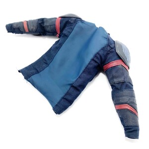 Op de afbeelding: Een zwart en blauw stoffen jack met rode accenten en gevoerde schouders. Het jack heeft een ritssluiting en een lange mouw.