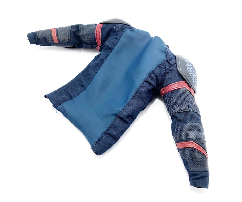 Op de afbeelding: Een zwart en blauw stoffen jack met rode accenten en gevoerde schouders. Het jack heeft een ritssluiting en een lange mouw.