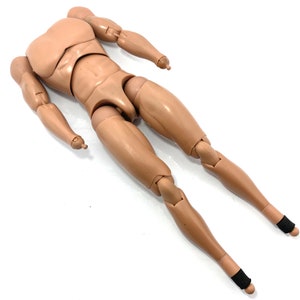 May include: A tan-colored articulated action figure body with a muscular physique. The figure has jointed arms, legs, and torso, allowing for various poses. Black bands are wrapped around the ankles. The figure is lying on a white surface.