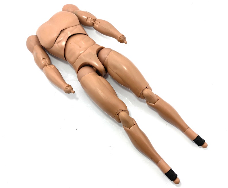 May include: A tan-colored articulated action figure body with a muscular physique. The figure has jointed arms, legs, and torso, allowing for various poses. Black bands are wrapped around the ankles. The figure is lying on a white surface.