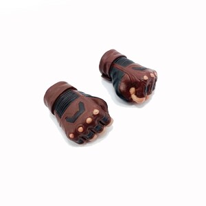 Op de afbeelding: Een paar bruine en zwarte leren handschoenen met vingerloze knokkels. De handschoenen hebben een textuurontwerp en zijn gemaakt voor actionfiguren.