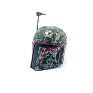 May include: A weathered green and red Boba Fett helmet with a black visor and a small antenna on top.