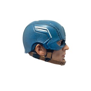 Puede incluir: Un casco de Capit&aacute;n Am&eacute;rica de pl&aacute;stico azul y blanco con una correa marr&oacute;n. El casco lo lleva puesto una persona, pero solo se ve el lado de la cara.
