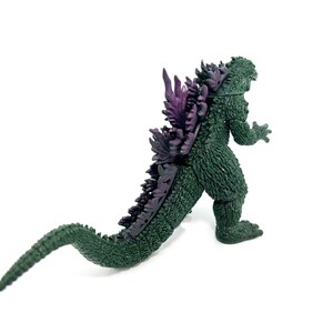 K&ouml;nnte beinhalten: Eine gr&uuml;ne Godzilla-Actionfigur mit lila R&uuml;ckenflossen und einem langen Schwanz. Die Figur ist in einer Laufhaltung dargestellt und zeigt ihre strukturierte Haut und ihr detailliertes Design. Ein Sammlerst&uuml;ck.