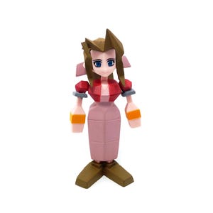 May include: A stylized figurine of a female character with brown hair, blue eyes, and a red top. The figure has a pink skirt and orange accents on the arms. The figurine is standing on a white surface.