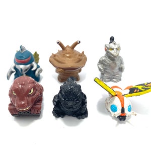 Puede incluir: Un conjunto de seis pequeñas figuras de plástico de diferentes monstruos. Las figuras están pintadas en varios colores, incluyendo azul, marrón, negro, rojo, blanco y amarillo. Las figuras miden aproximadamente 5 cm de alto.