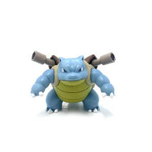 May include: A blue and green plastic toy figure of a Pokemon character, Blastoise, with two water cannons on its back.