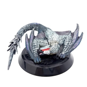 Könnte beinhalten: Detaillierte Drachenfigur mit grau-weißem Körper, rotem Maul und langem, stacheligem Schwanz. Der Drache posiert auf einem schwarzen, kreisförmigen Sockel. Die Flügel haben einen violett schillernden Schimmer. Die Figur ist ein Sammlerstück.