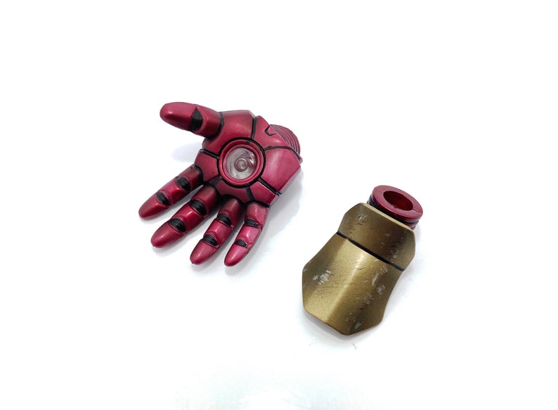 May include: A red and black Iron Man action figure hand with a gold and red forearm piece. The hand has a glowing light in the palm.