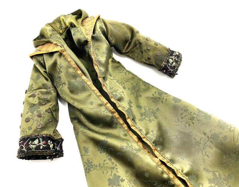 Op de afbeelding: Een lange, groene satijnen robe met een bloemenpatroon. De robe heeft gouden bies en decoratieve knopen. De mouwen hebben zwarte en gouden bies met kleurrijke borduurwerk.