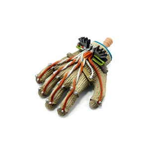 Puede incluir: Una mano rob&oacute;tica beige y marr&oacute;n con cables naranja y blanco. La mano tiene una peque&ntilde;a mu&ntilde;eca beige con un dispositivo mec&aacute;nico azul y verde unido a ella.