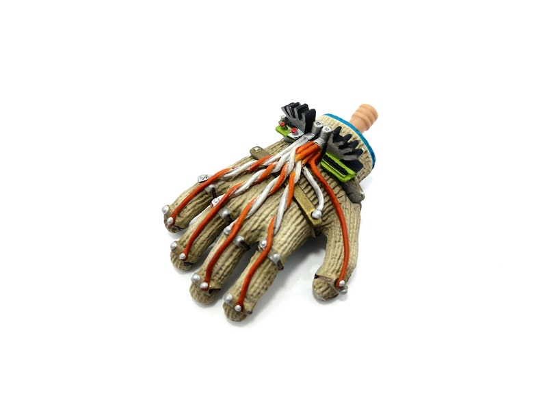 Puede incluir: Una mano rob&oacute;tica beige y marr&oacute;n con cables naranja y blanco. La mano tiene una peque&ntilde;a mu&ntilde;eca beige con un dispositivo mec&aacute;nico azul y verde unido a ella.