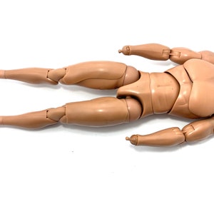 May include: A tan-colored articulated action figure body, lying on a white surface. The figure has jointed arms and legs, with black bands around the ankles. The figure is designed to be posed.