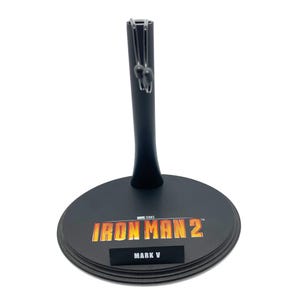 May include: Black plastic action figure stand with a round base. The base has the text "IRON MAN 2" in orange and yellow and "MARK V" in black.