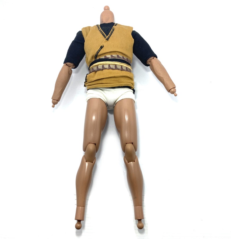 May include: An action figure with articulated limbs, dressed in a brown vest with a black undershirt and white underwear. The figure has a brown belt with a gold buckle.