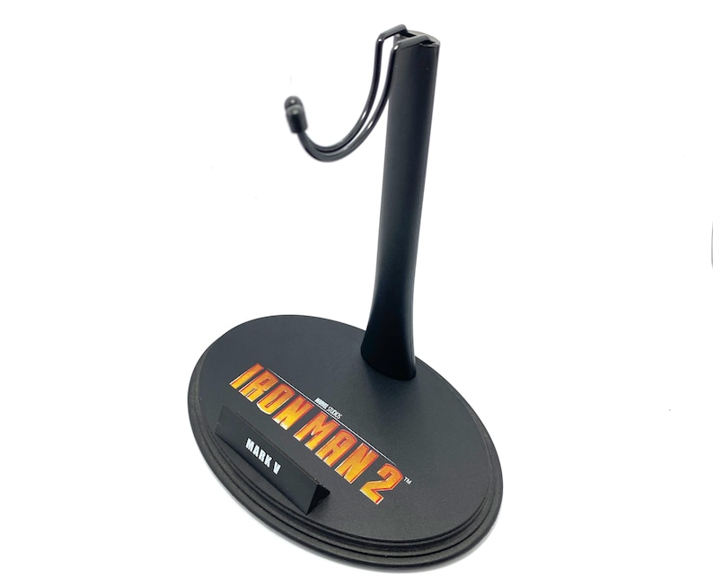 May include: Black plastic action figure stand with a metal hook. The base of the stand has the words "Iron Man 2" and "Mark V" printed on it.