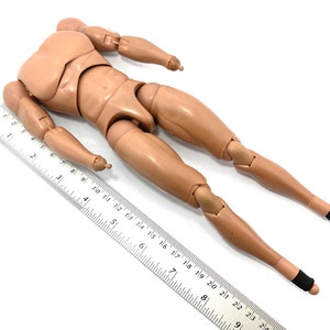 May include: A tan articulated action figure body with a ruler. The figure has a detailed muscular physique, with articulated joints at the shoulders, elbows, hips, and knees. The ruler is marked in inches and is used to measure the figure.