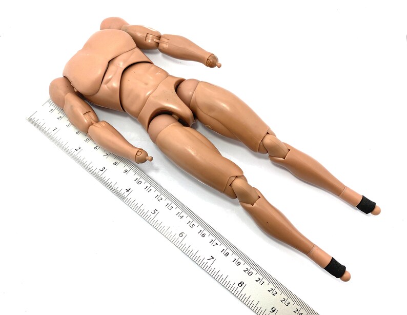 May include: A tan articulated action figure body with a ruler. The figure has a detailed muscular physique, with articulated joints at the shoulders, elbows, hips, and knees. The ruler is marked in inches and is used to measure the figure.
