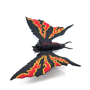 May include: A black insect-like figurine with a textured body and two large wings. The wings feature a jagged, flame-like pattern in bright red and yellow against a solid black background. The creature has a segmented torso and two thin antennae.