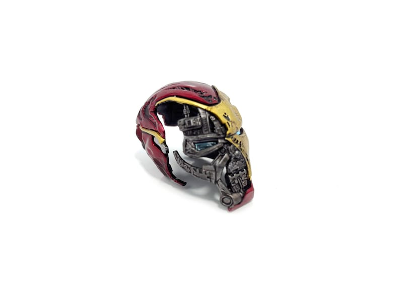May include: A detailed, partially disassembled Iron Man helmet, showcasing its internal mechanics. The helmet features a red and gold color scheme, with visible mechanical components and intricate detailing. The design is set against a plain white background.