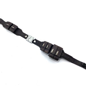 May include: A brown leather belt with a silver buckle and multiple pouches. The belt has a black button on the end.