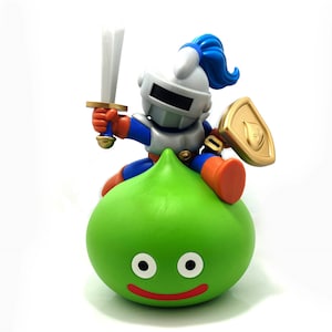 May include: A green slime monster with a smiling face and two large eyes. A small, blue and silver knight figure is riding on top of the slime monster, holding a sword and shield.