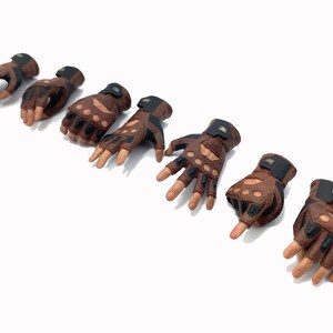 May include: Eight brown leather gloves with black accents and finger holes. The gloves have a textured surface and are designed for action figures.