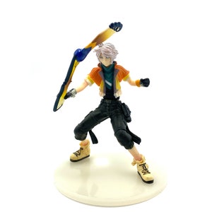 May include: A white-haired anime character figurine holding a yellow and blue weapon. The figurine is wearing a black and orange outfit and is standing on a white base.