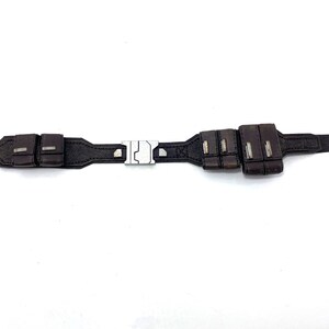 May include: A brown leather belt with a silver buckle and multiple pouches. The belt has a stitched design and a button on the end.
