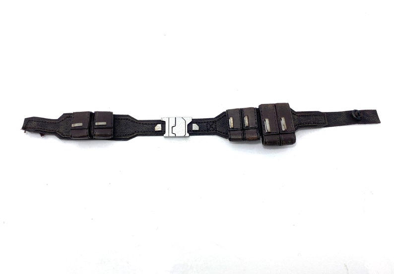 May include: A brown leather belt with a silver buckle and multiple pouches. The belt has a stitched design and a button on the end.