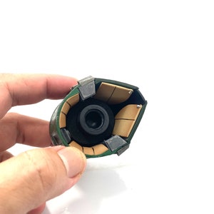 May include: Close-up of the inside of a green and brown helmet with a black lens. The helmet is made of multiple pieces that are held together with metal clips.
