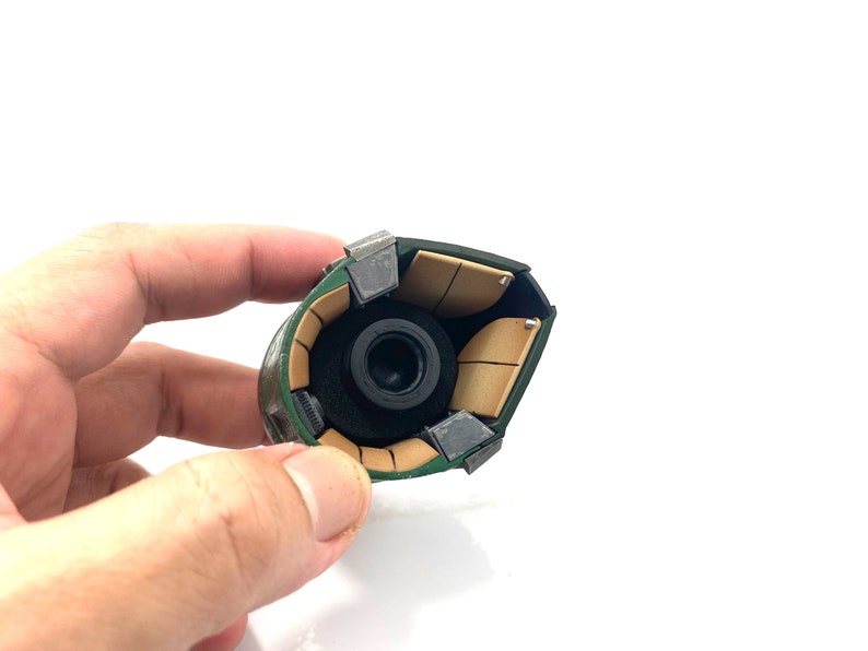 May include: Close-up of the inside of a green and brown helmet with a black lens. The helmet is made of multiple pieces that are held together with metal clips.