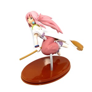 Op de afbeelding: Een beeldje van een vrouwelijk anime-personage met roze haar, gekleed in een witte en paarse outfit, rijdend op een bezem. Het beeldje staat op een bruine ovale basis en heeft een gedetailleerd ontwerp. Het personage staat in een dynamische pose.