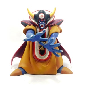 May include: A blue and yellow figurine of a demon with a single eye, horns, and a skull necklace. The demon is wearing a red and yellow robe and has its hands outstretched.