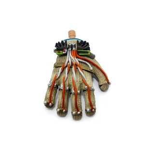 Puede incluir: Un guante beige y marr&oacute;n con cables naranja y blanco unidos a &eacute;l. El guante tiene un peque&ntilde;o dispositivo azul y verde unido a la parte posterior de la mano.