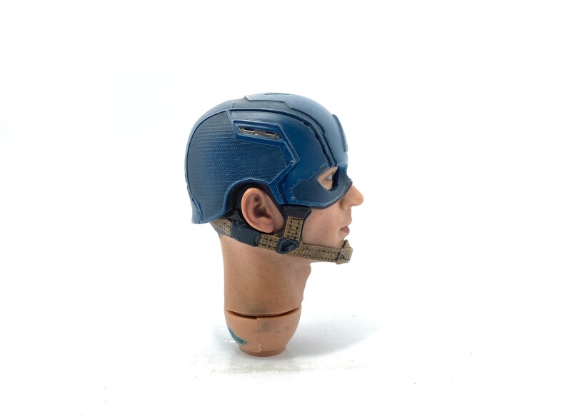 Op de afbeelding: Een blauw en zilver Captain America helm, een verzamelobject. De helm is een gedetailleerde replica, met een textuurontwerp en riemen. Hoofd en nek zijn ook zichtbaar.