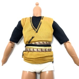 May include: A yellow sleeveless shirt with black trim and a brown and gold belt. The shirt is worn over a black short-sleeved shirt.