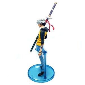 Pu&ograve; includere: Statuetta di un personaggio della serie anime One Piece. La figura indossa una giacca gialla e nera, jeans blu e un cappello bianco con pois neri. Tiene una katana ed &egrave; montata su un supporto blu.