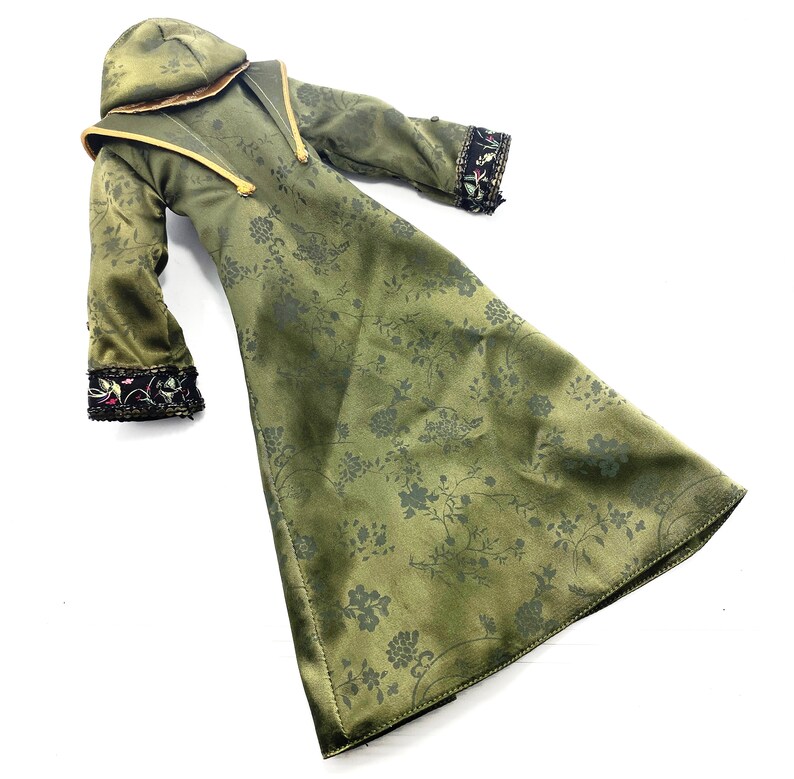 Op de afbeelding: Een lange groene robe met een bloemenpatroon en zwarte en gouden versieringen. De robe heeft een capuchon en lange mouwen.