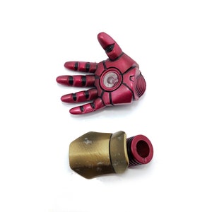 May include: Red and gold plastic action figure hand and forearm. The hand is open and has a red light in the palm. The forearm is gold and has a red plastic connector.
