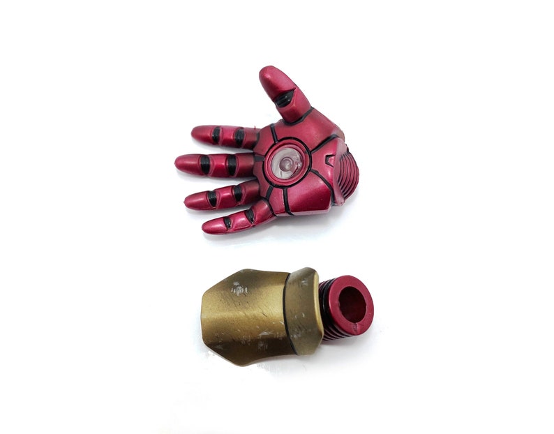 May include: Red and gold plastic action figure hand and forearm. The hand is open and has a red light in the palm. The forearm is gold and has a red plastic connector.