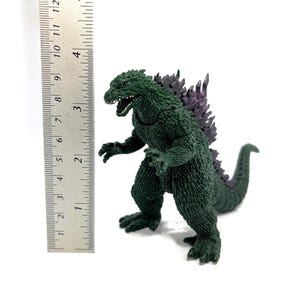K&ouml;nnte beinhalten: Eine gr&uuml;ne Godzilla-Figur mit lila R&uuml;ckenflossen, etwa 10 cm hoch, steht neben einem Lineal. Das Spielzeug hat einen ge&ouml;ffneten Mund und steht auf einer wei&szlig;en Oberfl&auml;che.