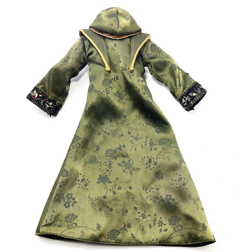 Op de afbeelding: Een lange groene robe met een bloemenpatroon en een capuchon. De robe heeft zwarte en gouden bies en een gouden koord.