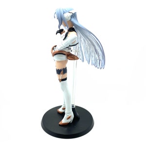May include: A figurine of a character with long, pale blue hair and a white and black outfit. The figure is on a black circular base, with a clear support rod. The figure's boots have brown accents.
