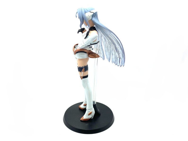 May include: A figurine of a character with long, pale blue hair and a white and black outfit. The figure is on a black circular base, with a clear support rod. The figure's boots have brown accents.