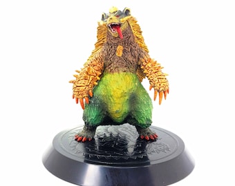 May include: A detailed figurine of a monster with a bear-like body, featuring a brown torso, green lower body, and orange spiky arms. The monster has a yellow mane, red tongue, and is mounted on a black circular base with a decorative pattern.